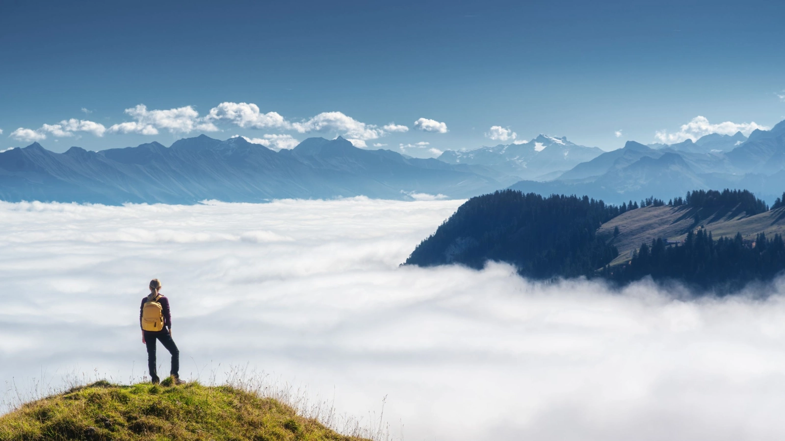 Woman with backpack on mountain ridge above a sea of clouds