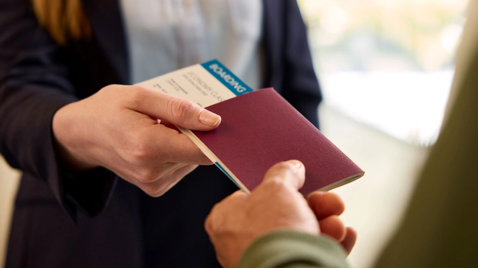 A traveller hands a passport and boarding pass to an airport check-in agent.