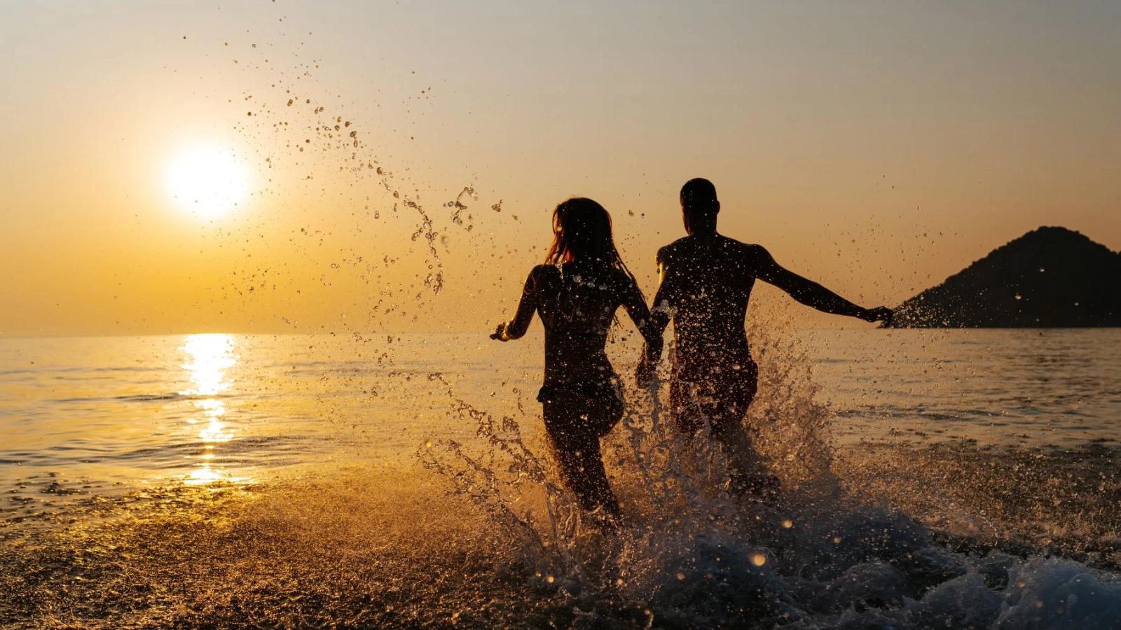 Young couple running into the sea at sunset