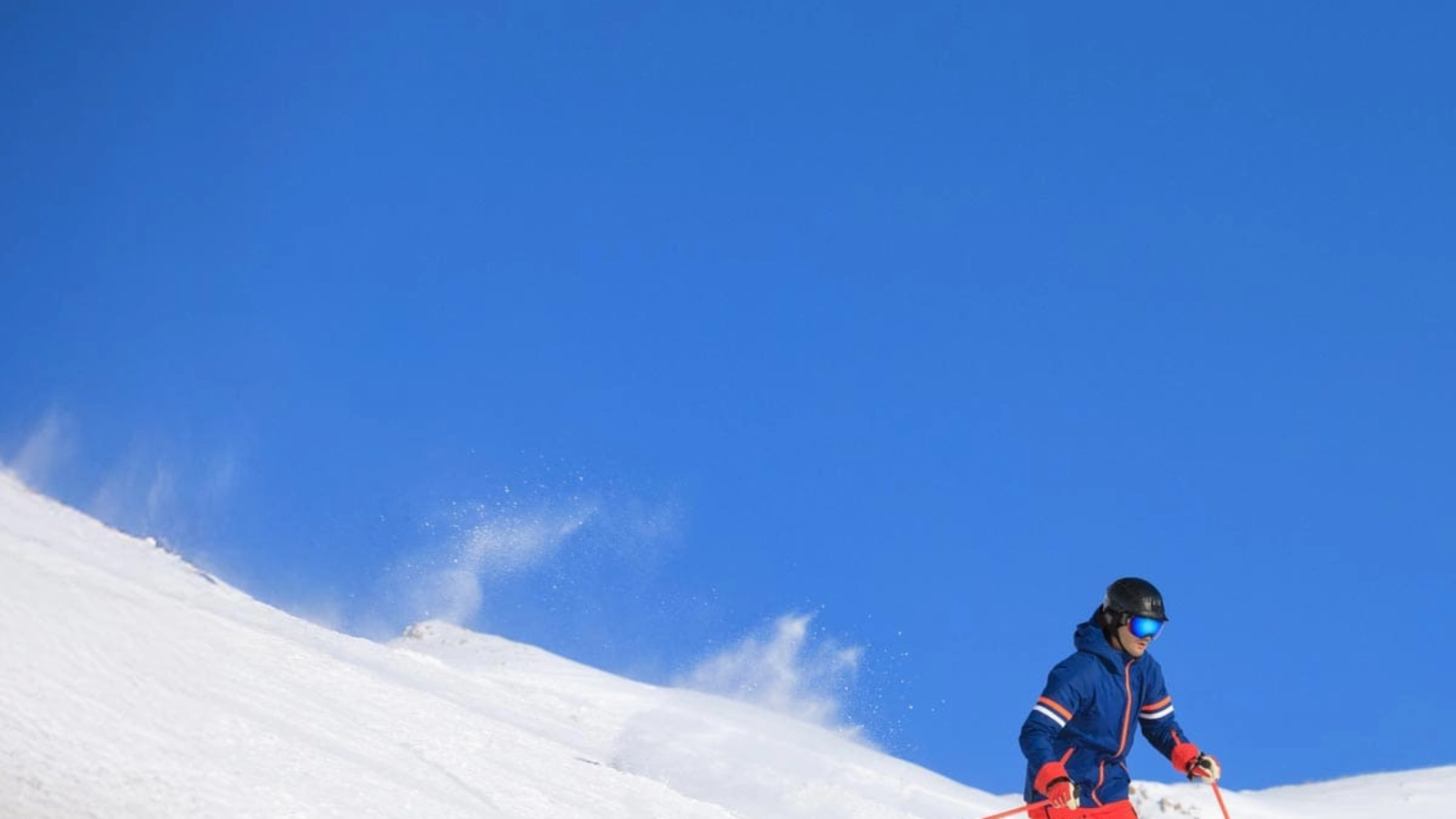 A person skiing in a blue jacket and red trousers