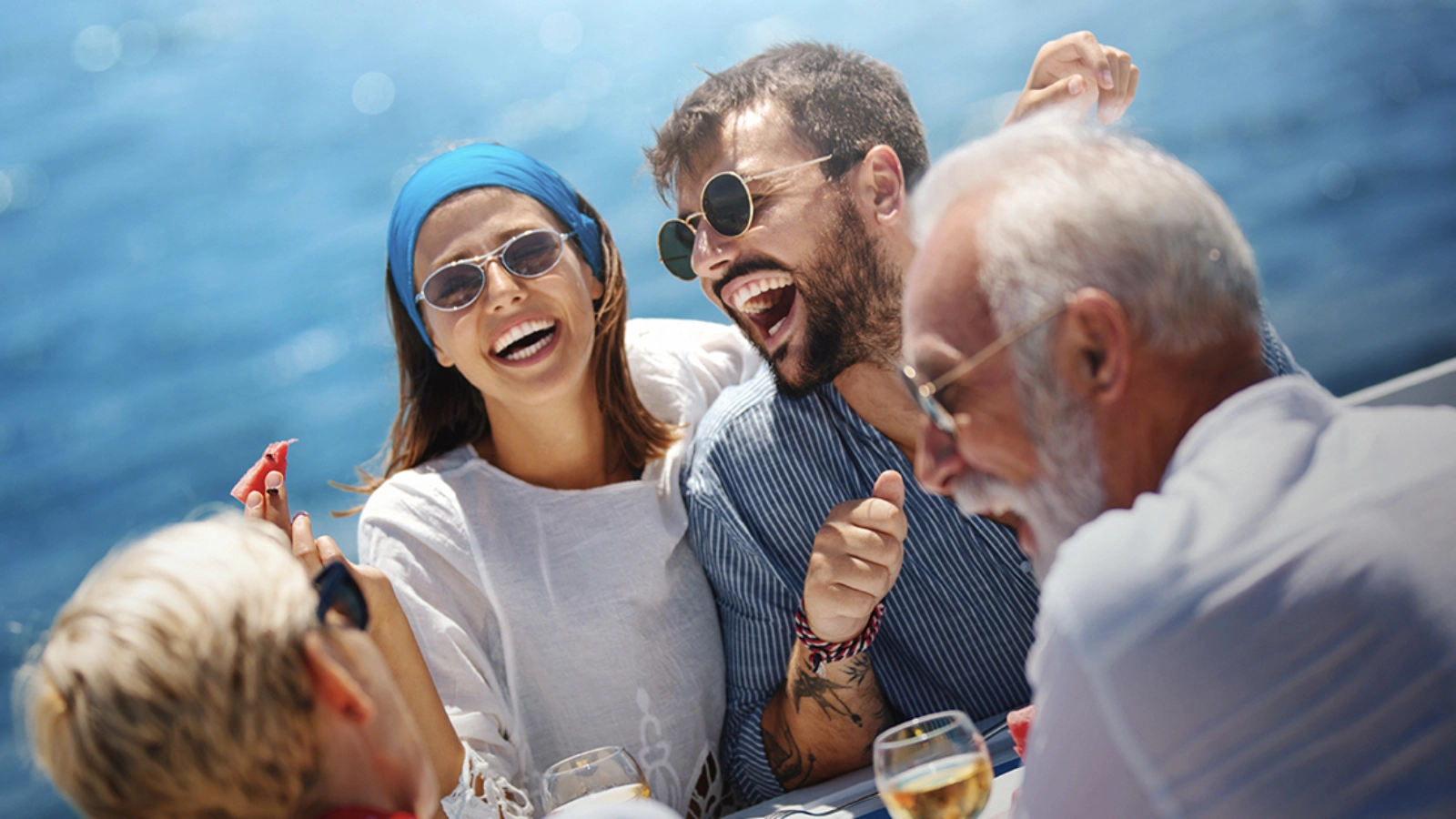 Group of friends laughing and enjoying drinks together on a boat at sea.